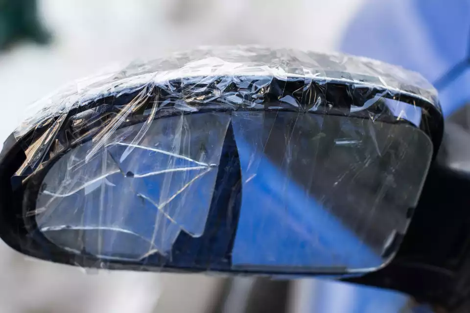 damaged and cracked glass of a side view mirror, wrapped in plastic